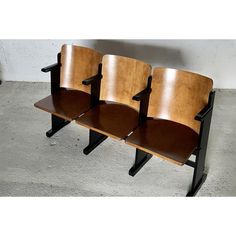 three wooden chairs sitting next to each other on top of cement floored area with white wall in the background