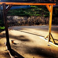 an empty swing frame in the middle of a dirt area with grass and rocks behind it