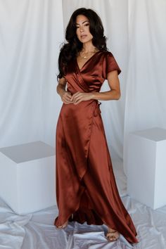 a woman standing in front of a white backdrop wearing a long brown dress and sandals