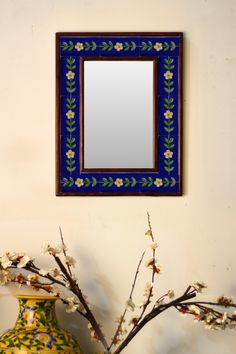 a blue and yellow vase sitting next to a mirror on a wall with flowers in it