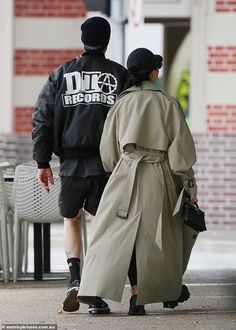 a man and woman walking down the street wearing trenchs, hats, and jackets