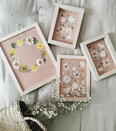 four framed pictures with flowers on them sitting next to a wicker basket and straw hat