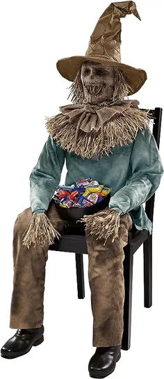 a scarecrow sitting on a chair with a bowl of candy in his lap and wearing a hat