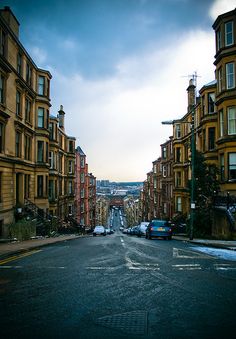 an empty city street with cars parked on both sides and buildings in the back ground