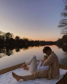 a man sitting on top of a wooden dock next to a body of water at sunset