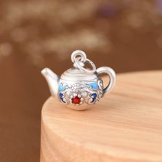 a silver teapot with a red glass bead on it's side sitting on top of a wooden table