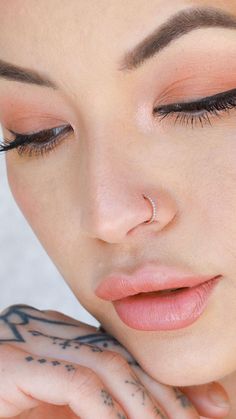 a close up of a woman with tattoos on her arm and face, wearing a nose ring