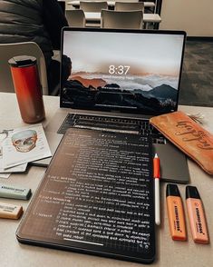 an open laptop computer sitting on top of a table next to some pens and pencils