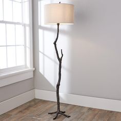 a floor lamp with a white shade on it in front of a window and wood floor