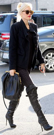 a woman walking down the street carrying a handbag and wearing high heeled boots