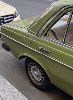 an old green car parked on the side of the road next to a white car