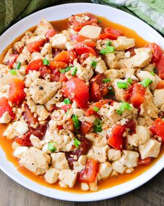 a white plate topped with chicken and tomatoes covered in sauce on top of a wooden table