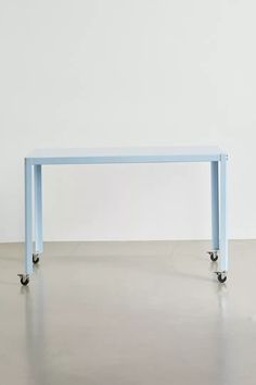 a blue table sitting on top of a metal floor next to a white wall with wheels