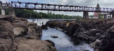 people are walking across a bridge over a small river that is surrounded by large rocks