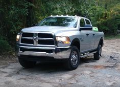 a silver ram truck parked on top of a dirt road next to some green trees