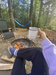 a person sitting in front of a campfire holding a mug