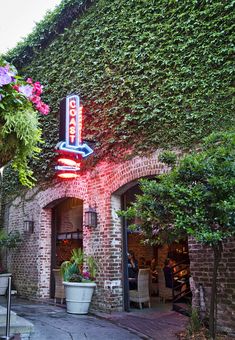 a brick building with a neon sign on it's side and potted plants in front