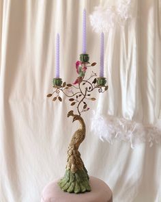 a pink stool with a peacock on it and some candles in the back ground, next to a white backdrop