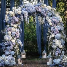 an outdoor wedding ceremony with blue drapes and white hydrangeas on the arch