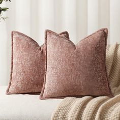 two pillows sitting on top of a white couch next to a potted green plant