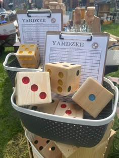 several wooden dices are stacked in a bucket on the grass, with two signs attached to them