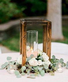 a wooden lantern with flowers and candles on a white table cloth at a wedding reception