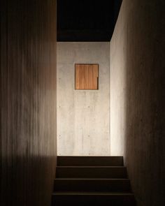 stairs leading up to a small window in a room with concrete walls and wooden steps