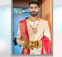 a man wearing a white and red outfit with orange dupatta standing in front of a doorway