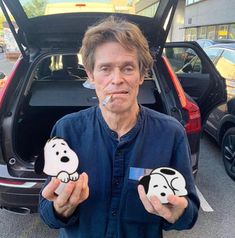 a man standing in front of a car holding up two snoopy dog magnets