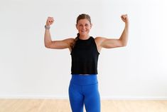 a woman in blue leggings and a black top is flexing her muscles