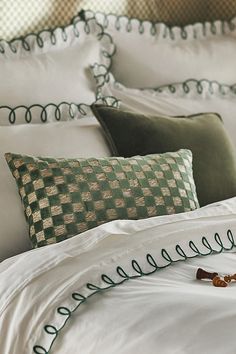 a bed with white sheets and green decorative pillow cases on it, along with a pair of scissors