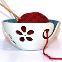 a white bowl with red yarn and knitting needles in it, sitting on a table