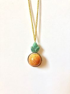 An orange ceramic bead is surrounded by a golden circle and topped with a green glass leaf. The entire charm is 1.5" long. Orange Circle, Orange Ceramic, Orange Necklace, Golden Circle, Orange You Glad, Circle Necklace, Ceramic Beads, Green Glass, Charm Necklace