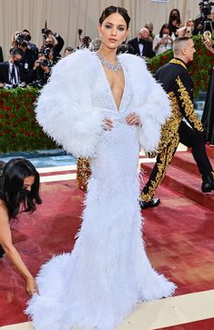 a woman in a white feathered dress standing on a red carpet