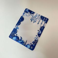 a blue and white square shaped glass plate on a table with beads hanging from it's sides