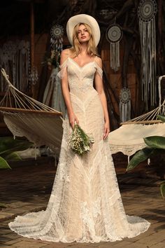 a woman in a white dress and hat standing next to a hammock with flowers