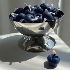 blueberries in a silver bowl next to a candle on a white tablecloth with shadows