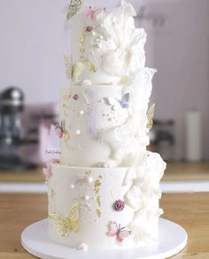 a three tiered wedding cake decorated with butterflies and flowers on a white plate sitting on a wooden table