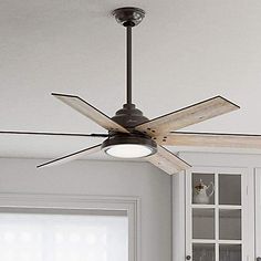 a ceiling fan in a kitchen with white cabinets and cupboards behind it, the light is on