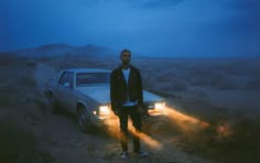 a man standing next to a car in the middle of a dirt road at night