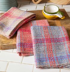 two pieces of cloth sitting on top of a wooden cutting board next to a bowl