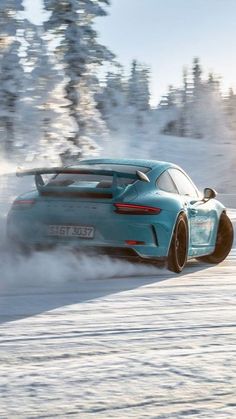 a blue sports car driving down a snow covered road with trees in the back ground