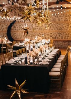 a long table is set up with black linens and gold stars hanging from the ceiling