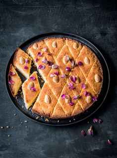 a cake with slices cut out on a black plate next to some nuts and flowers