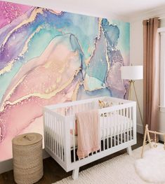 a white crib in front of a large wall mural with pink, blue and gold paint