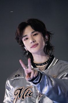 the young man is making a peace sign with his hand while wearing a silver jacket