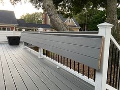 a deck with white railings and trees in the back ground, next to a house