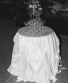 a table topped with lots of glasses on top of a white cloth covered round table