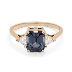 A three stone engagement ring with an emerald cut and emerald shape grey spinel center stone with two white diamond trillion side stones set in yellow gold. Anna Sheffield, Trillion Diamonds, Spinel Ring, Three Stone Ring, Pink Morganite, Grey Diamond, Champagne Diamond, Three Stone Rings, New Classic