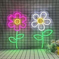 two neon flowers sitting next to each other in front of a wall with grids